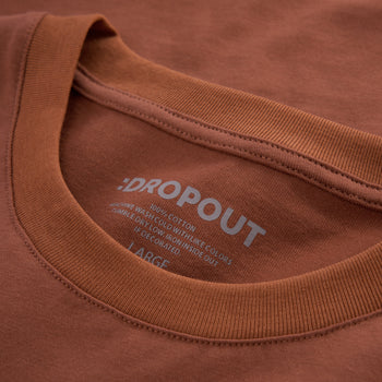 Close-up of a rust-brown crewneck t-shirt showing the inner collar print with the brand ':DROPOUT' and size 'LARGE'.