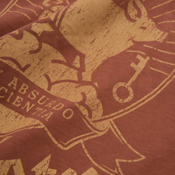 Close-up of a distressed graphic print on a terracotta red fabric, featuring a tan illustration and the text 'ABSURDO SCIENTIA'.