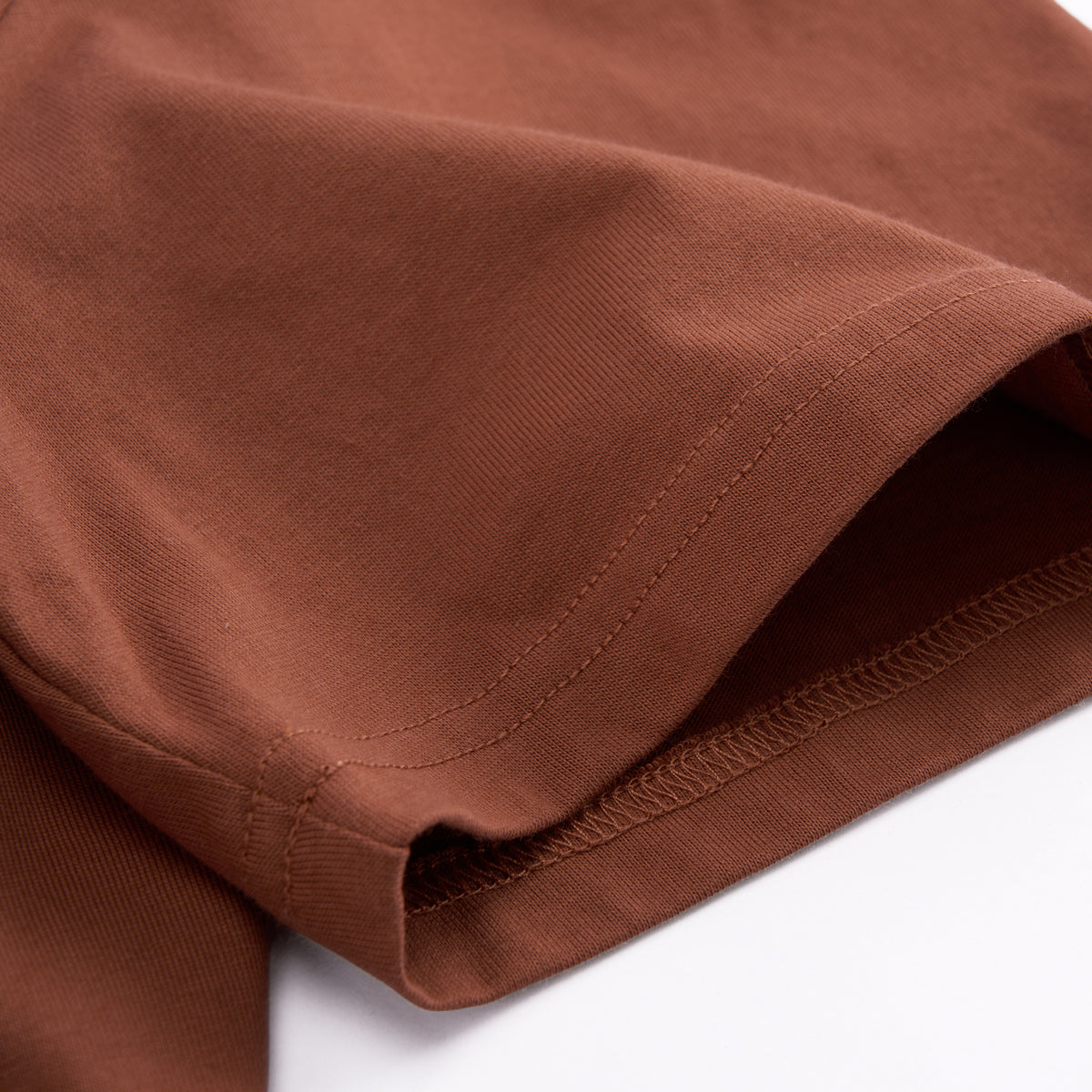 Close-up of a brown fabric garment, showing the texture and hem stitching detail against a white background.