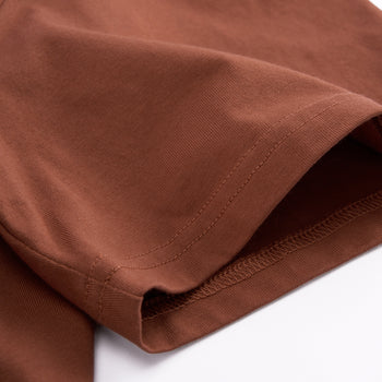 Close-up of a brown fabric garment, showing the texture and hem stitching detail against a white background.